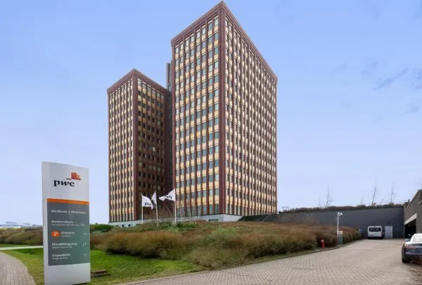Twee hoge kantoorgebouwen van PwC aan de Fascinatio Boulevard in Rotterdam met vlaggen en bewegwijzering op de voorgrond.